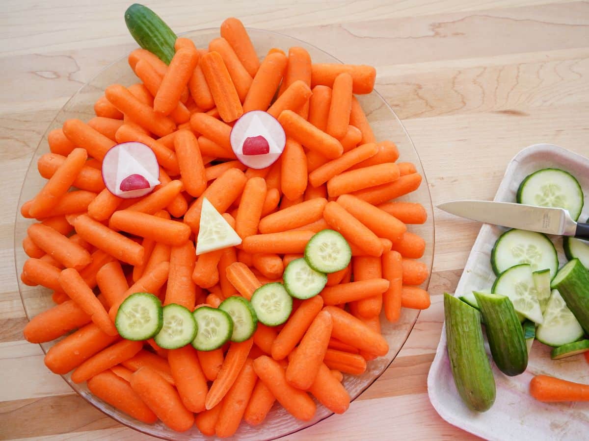 pumpkin vegetable tray with scraps of cucumber and carrots beside it on a cutting board