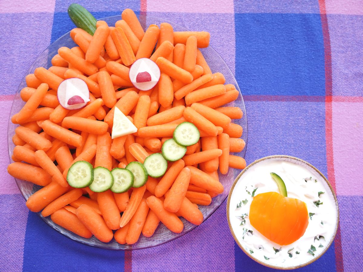 pumpkin veggie tray with bowl of vegetable dip beside on a plaid table cloth
