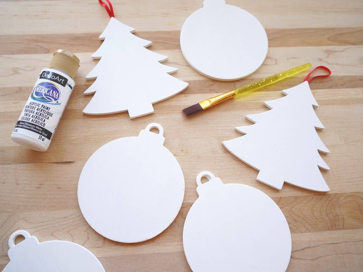 6 wooden christmas ornaments painted white with acrylic paint bottle and paintbrush