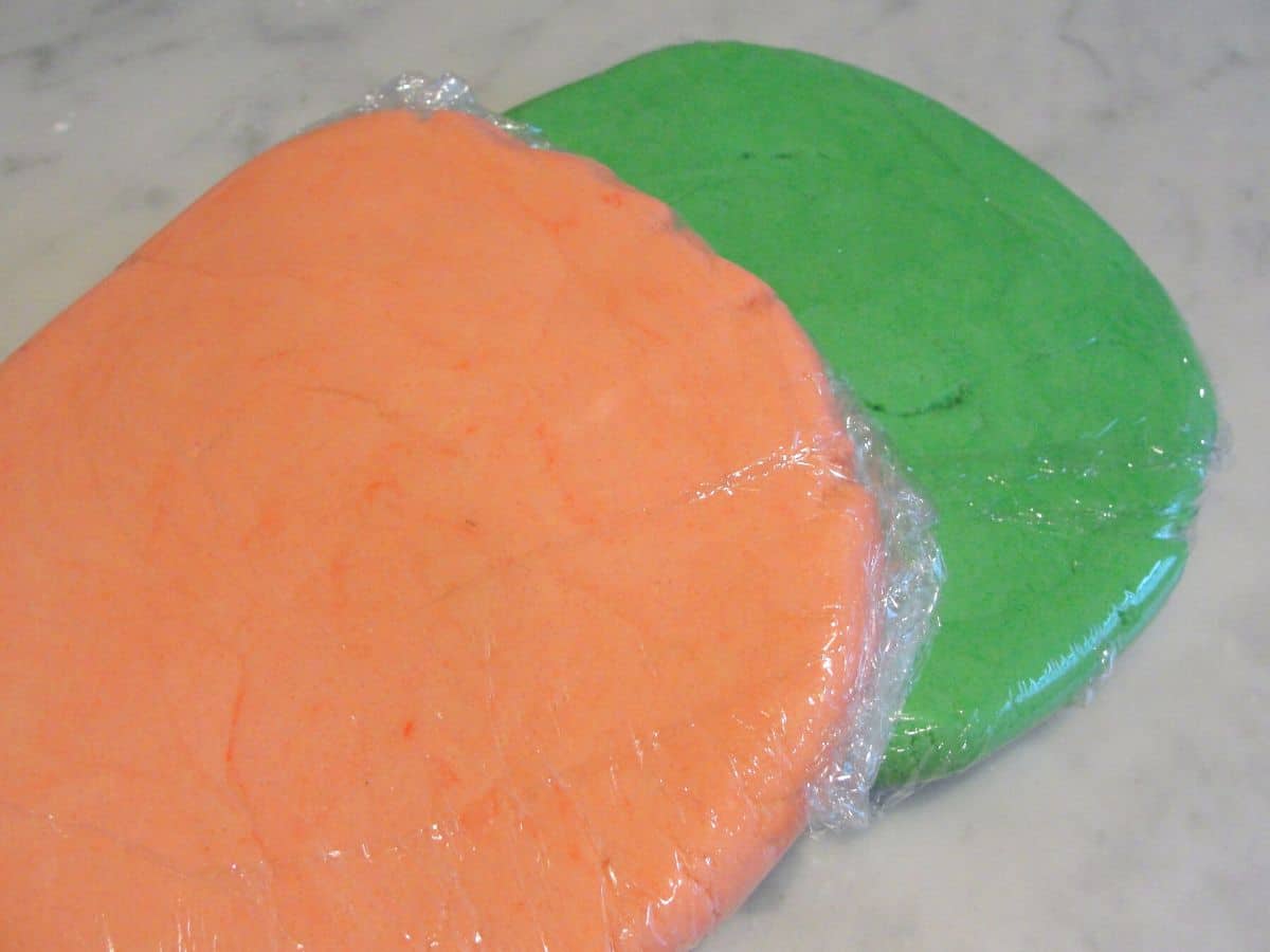 disks of pink and green christmas cookie dough wrapped in plastic wrap