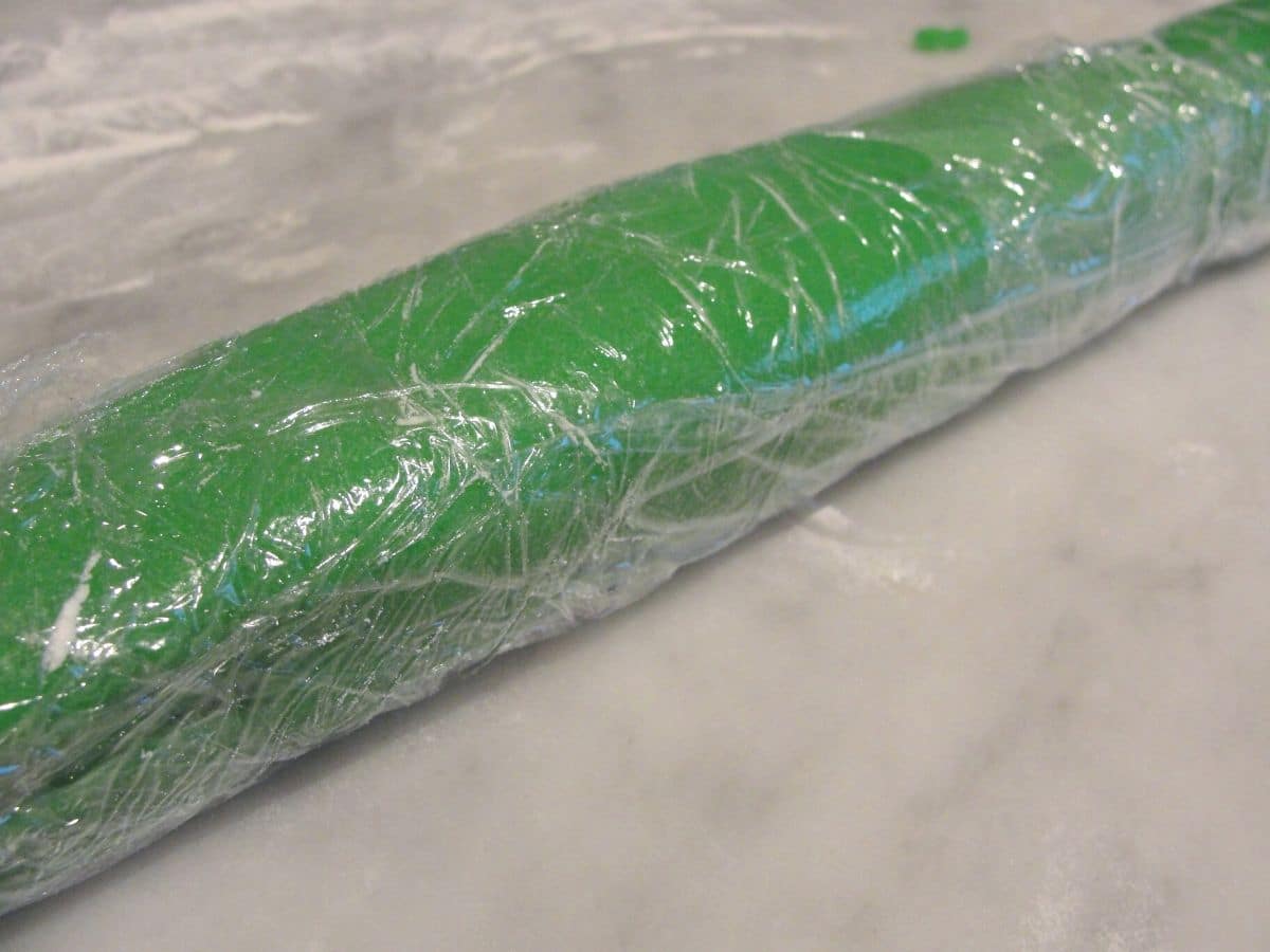 long roll of christmas cookie dough wrapped in plastic wrap on marble counter