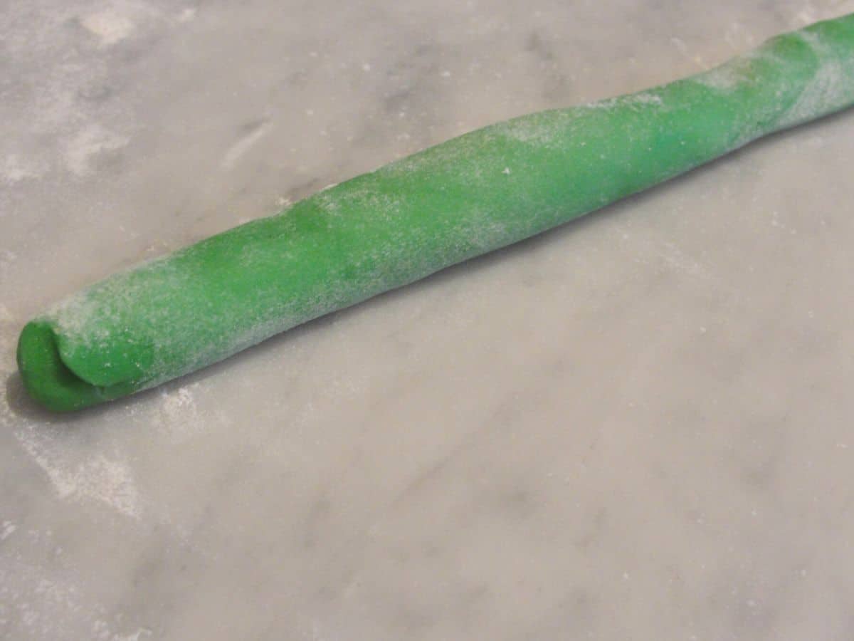 long roll of green christmas cookie dough on marble counter