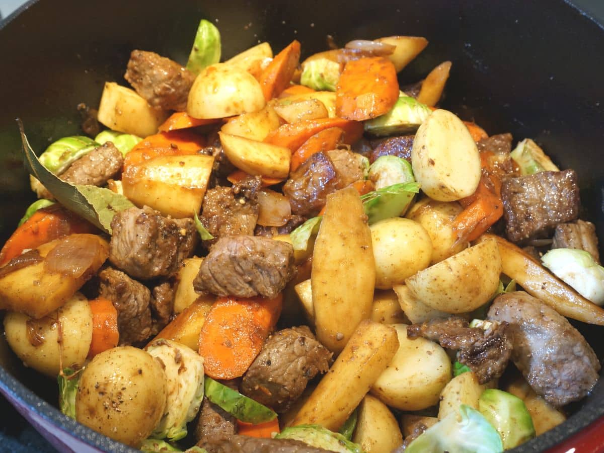 cooked stewing beef, potatoes, carrots, brussel sprouts and bay leaf in pot