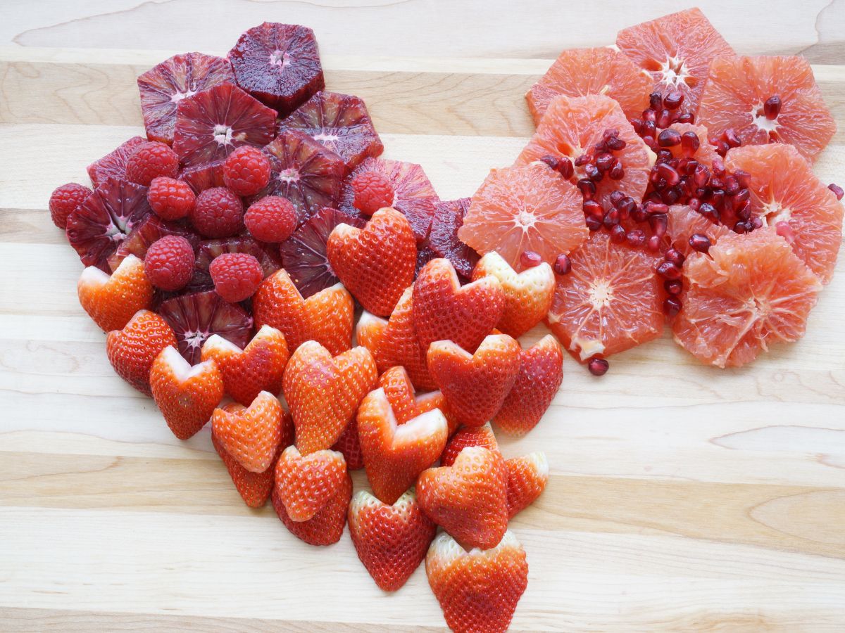 heart shaped pile of sliced blood orange, grapefruit, heart shaped strawberries, raspberries and pomegranate