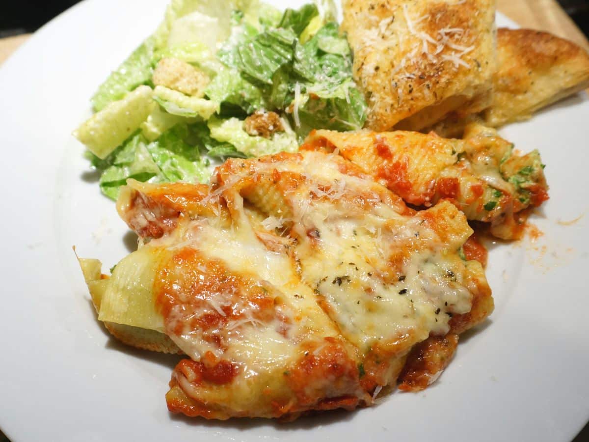 plate with stuffed pasta jumbo shells with ricotta and spinach filling and salad and slice of garlic bread