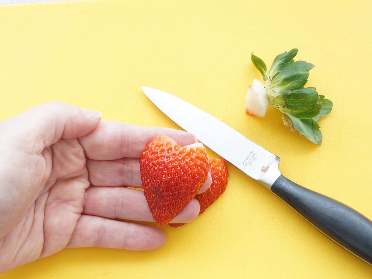 strawberry heart in hand with paring knife in background