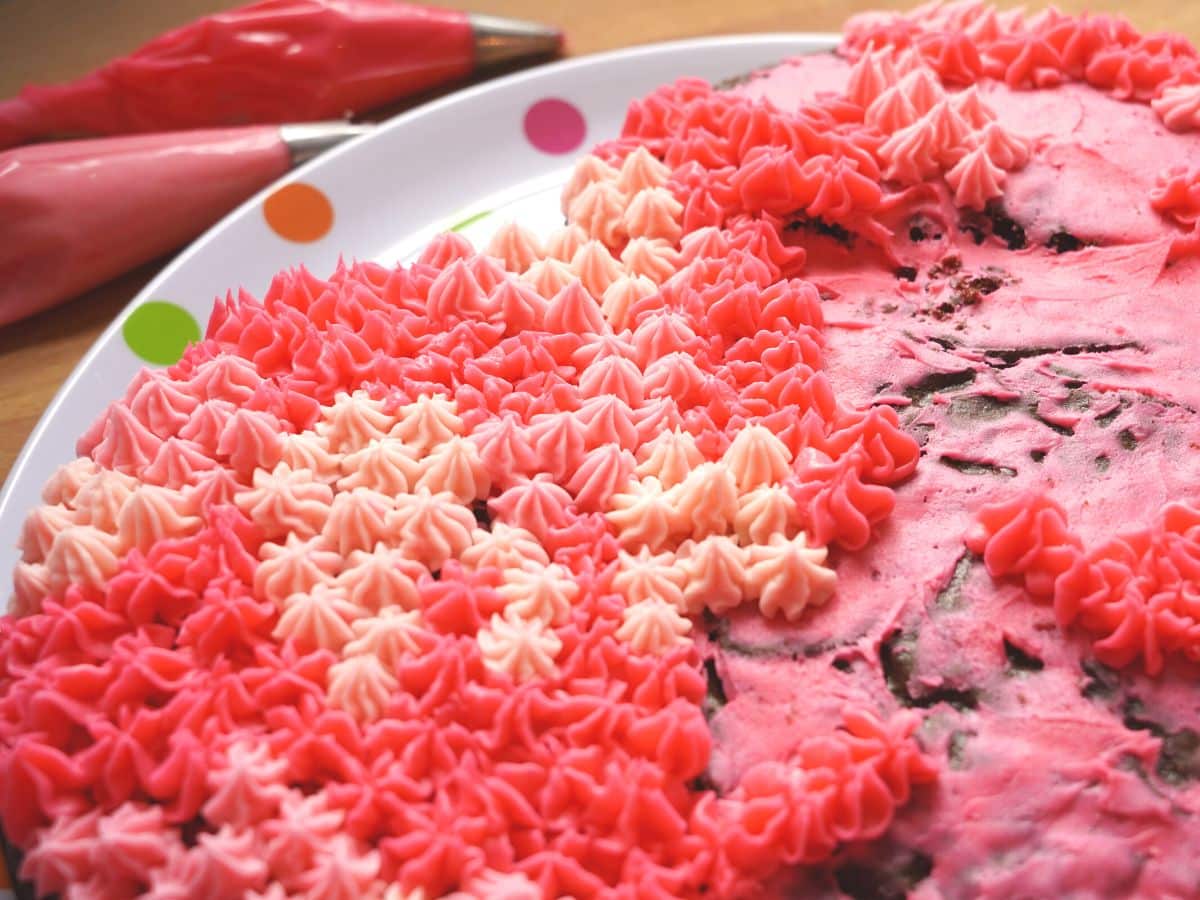 two piping bags with pink icing and close up of chocolate cake covered in pink icing drop flowers