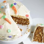 carrot cake with cream cheese frosting sliced with cake on plate. fondant bunny and fondant carrots on top