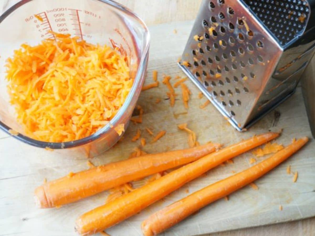 carrots being peeled on cutting board with grater and measuring  bowl
