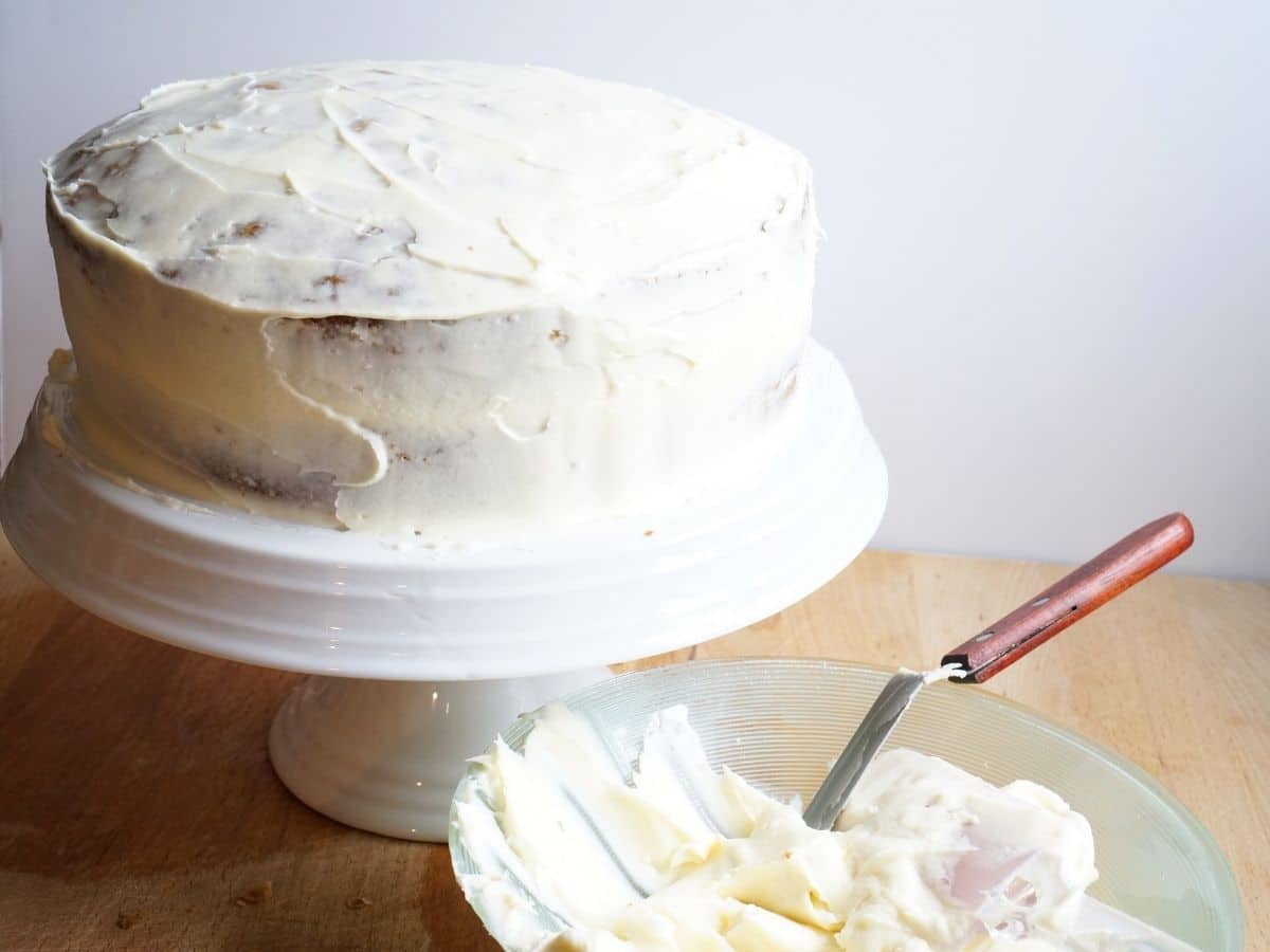 crumb coat of cream cheese frosting on carrot cake sitting on cake stand