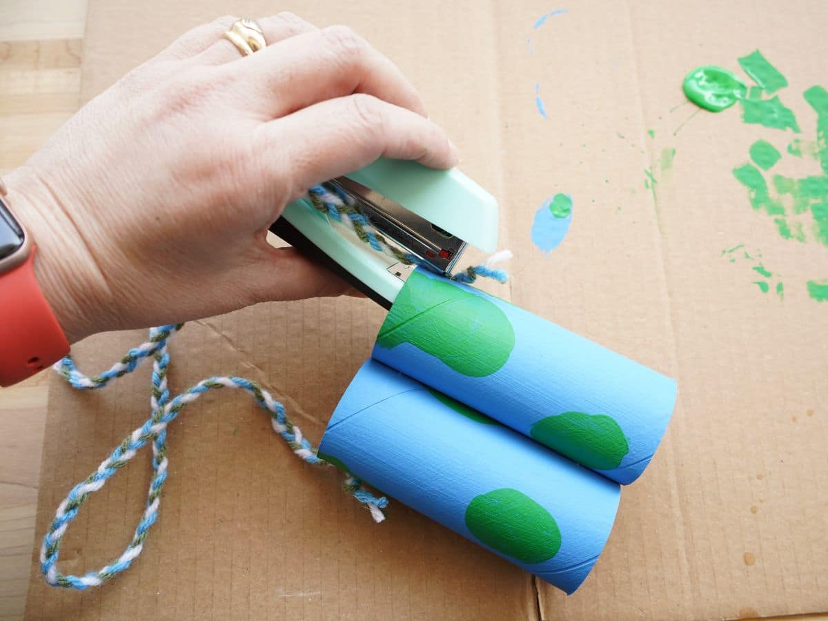 painted toilet paper roll binoculars' yarn being stapled on