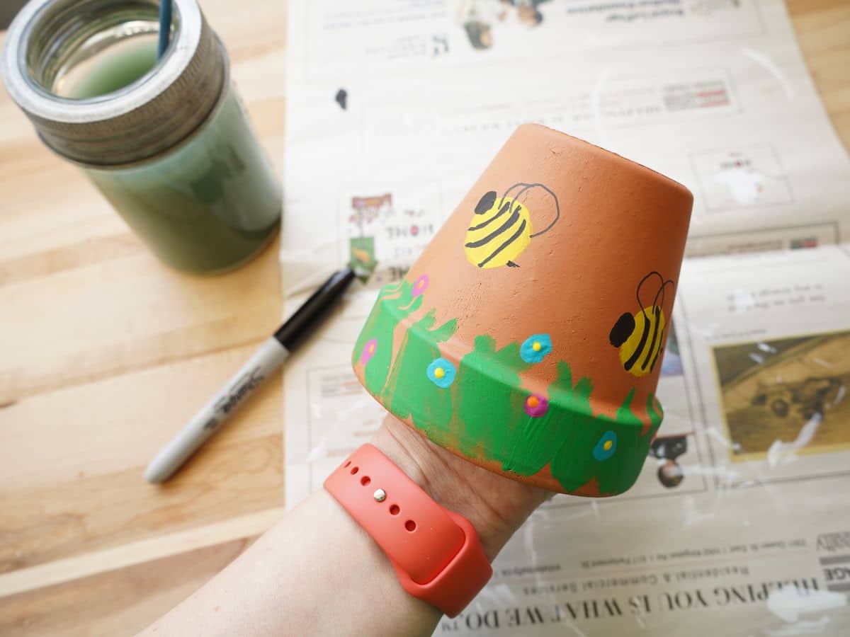 bees, flowers and grass painted on terra cotta pot with marker and hand