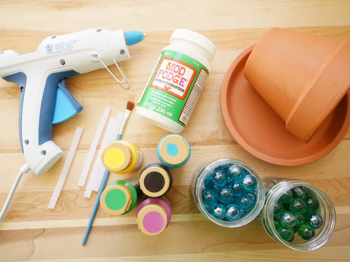 supplies for making terracotta pot bee bath - glue gun, paint, marbles, pot and bottle of sealant