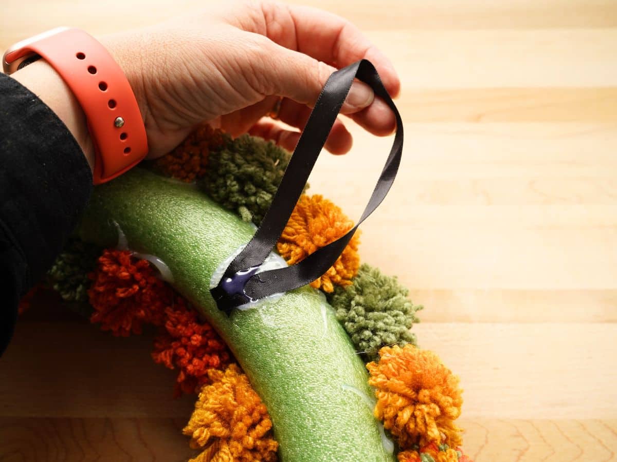 loop of ribbon glued on the back of a fall pom pom wreath with hand holding loop