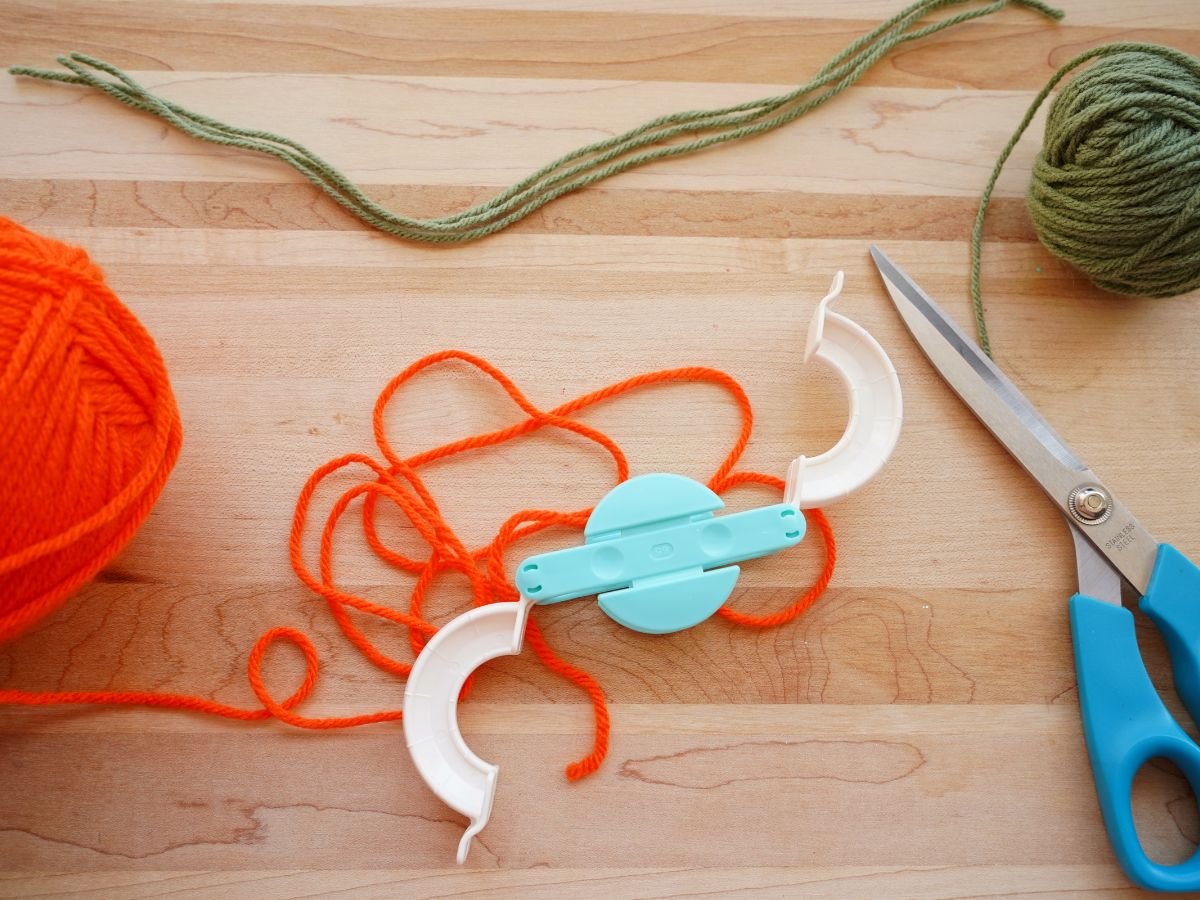 supplies for making pompom pumpkins - tool, yarn and scissors