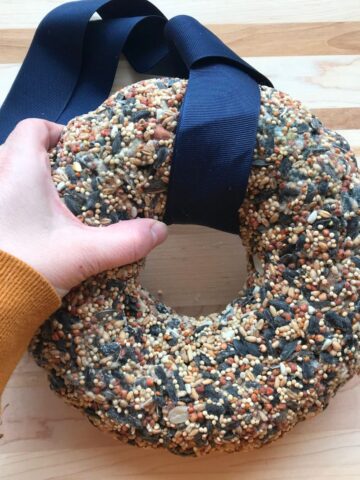 woman's hand holding a diy birdseed wreath on a wooden tabletop