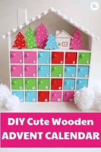 DIY Wooden advent calendar idea craft project - image of colorful painted wooden advent calendar with cardboard christmas trees and a cabin in the upper area of the calendar