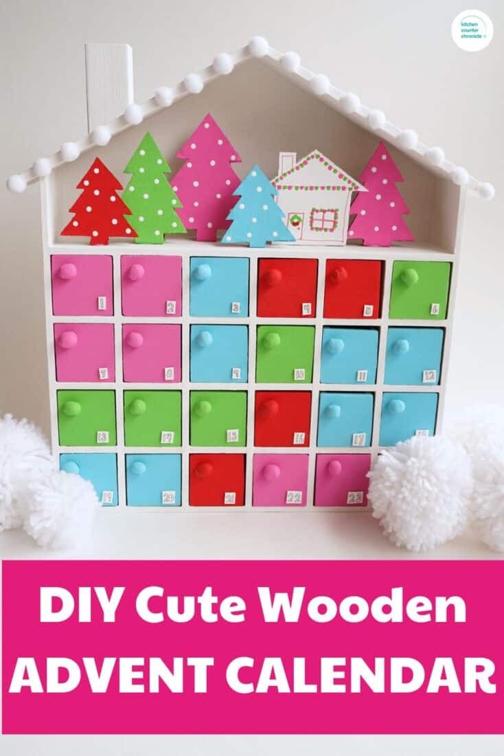 DIY Wooden advent calendar idea craft project - image of colorful painted wooden advent calendar with cardboard christmas trees and a cabin in the upper area of the calendar