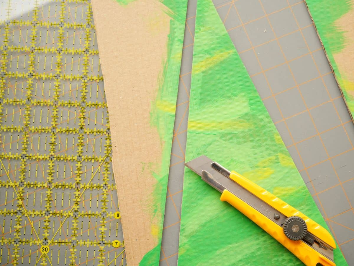 cardboard painted christmas tree with ruler and utility knife cutting out tree shape