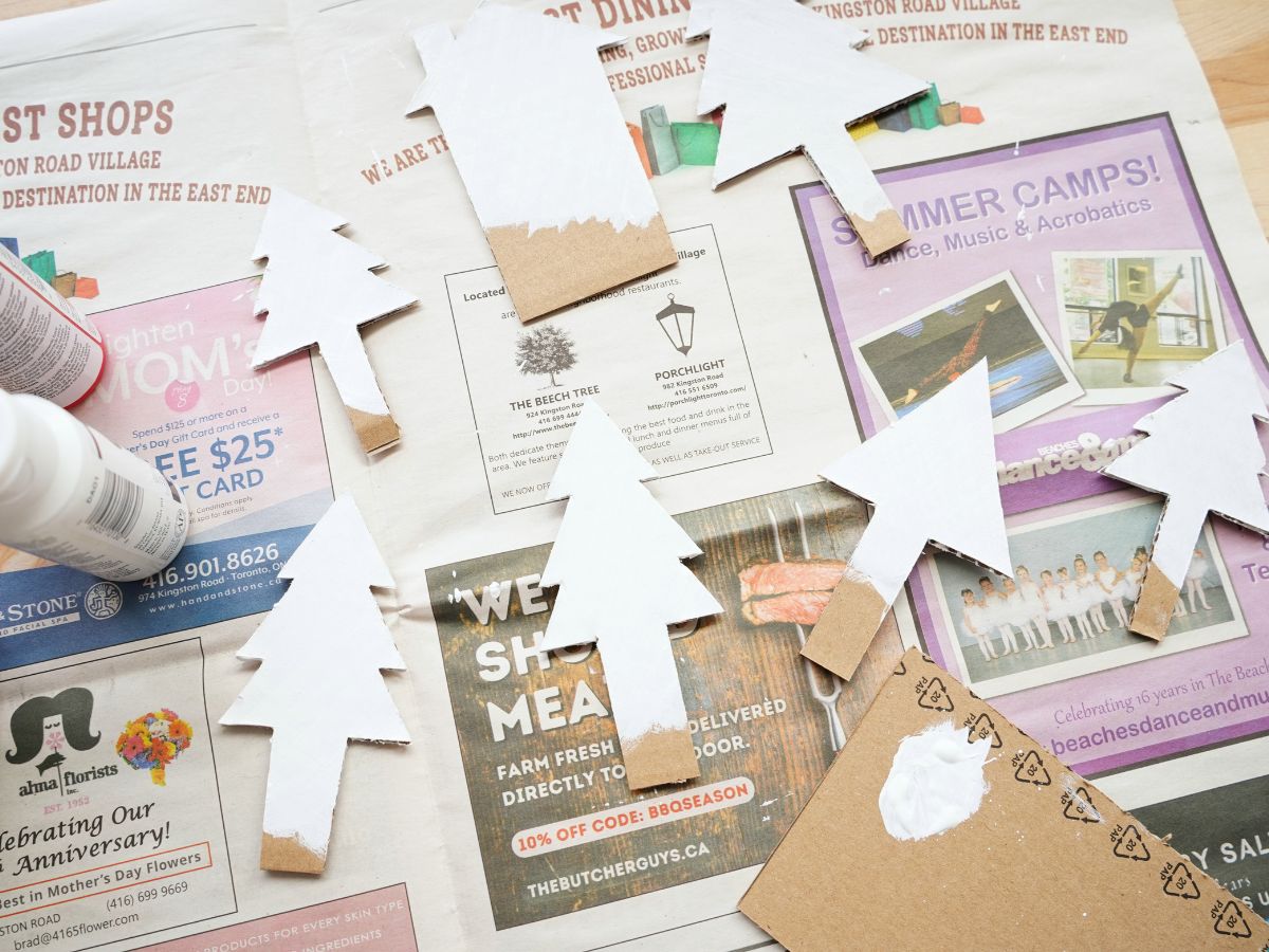 cardboard trees and cabin painted white on newspaper