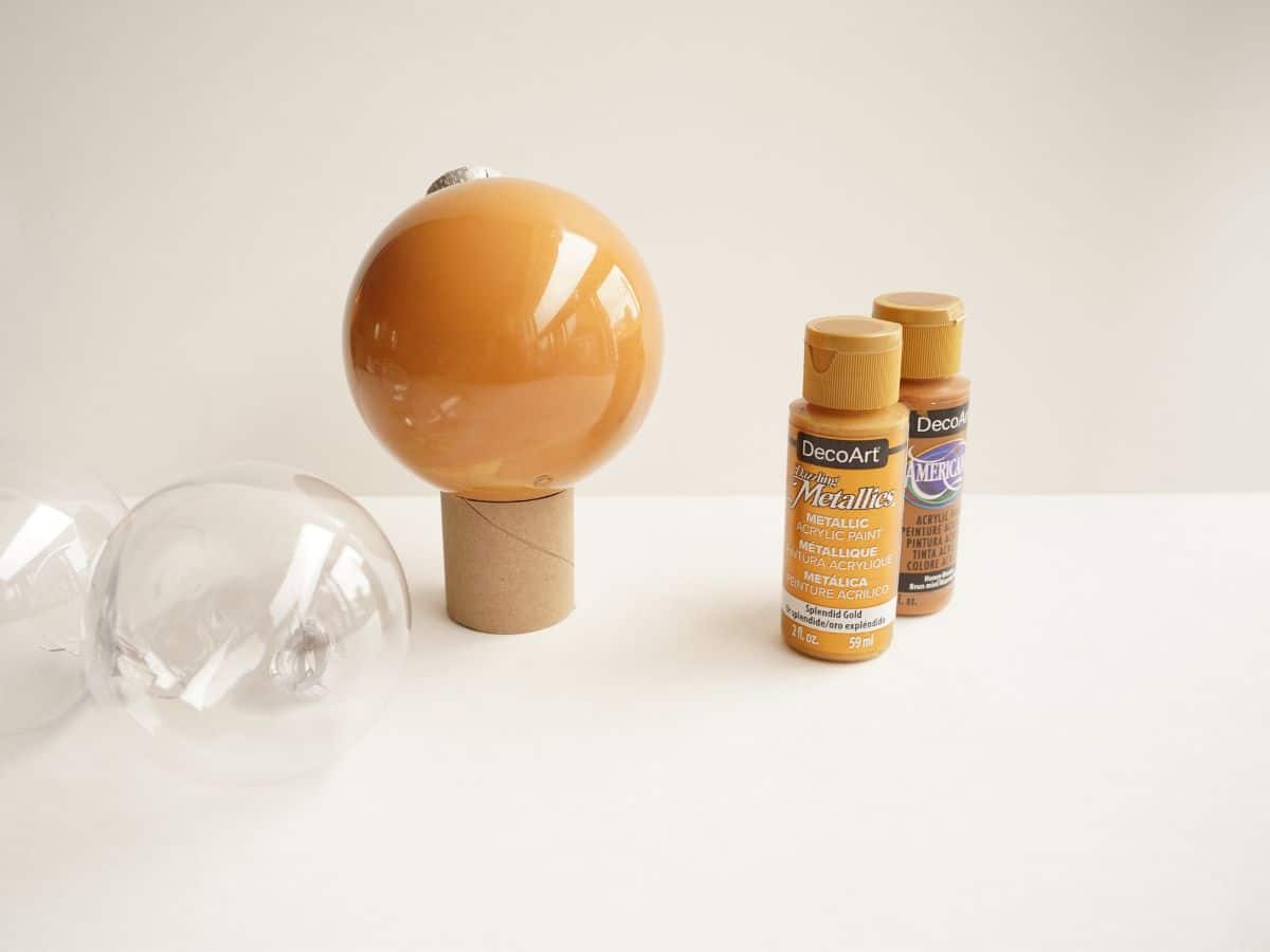 reindeer ornament ball in toilet paper roll stand with two brown paints beside 