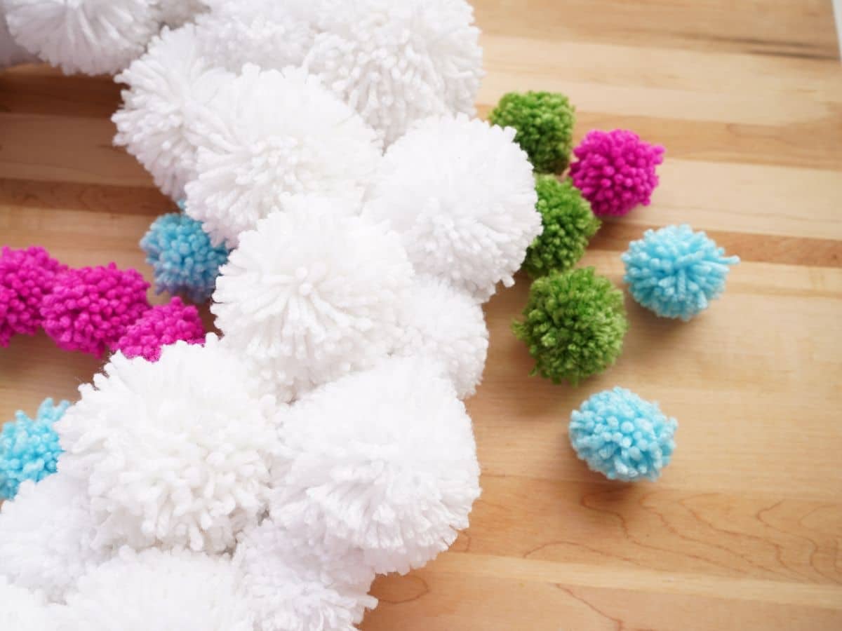 christmas white pompom wreath with a pile of small colorful pompoms