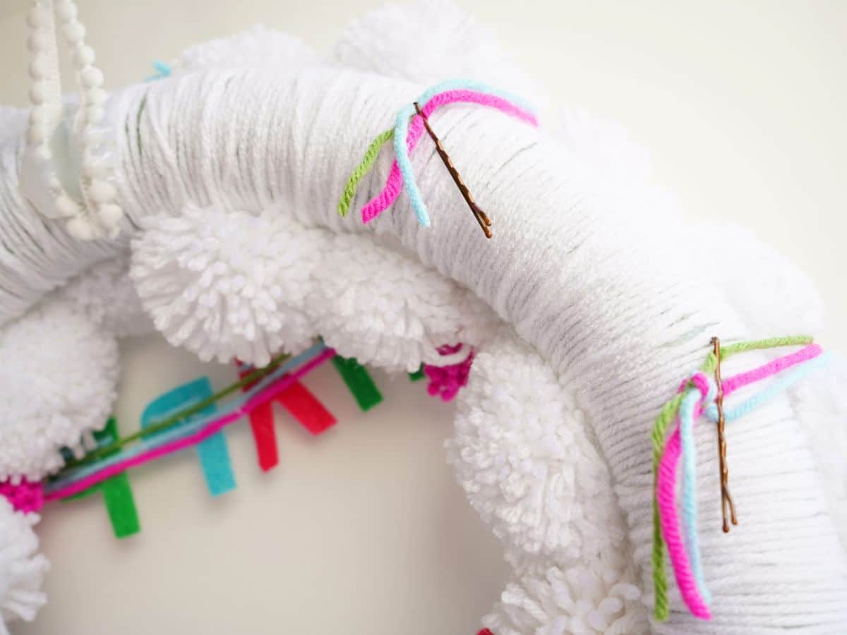 close up of backside of white pompom wreath with bobby pins securing the yarn garland in place