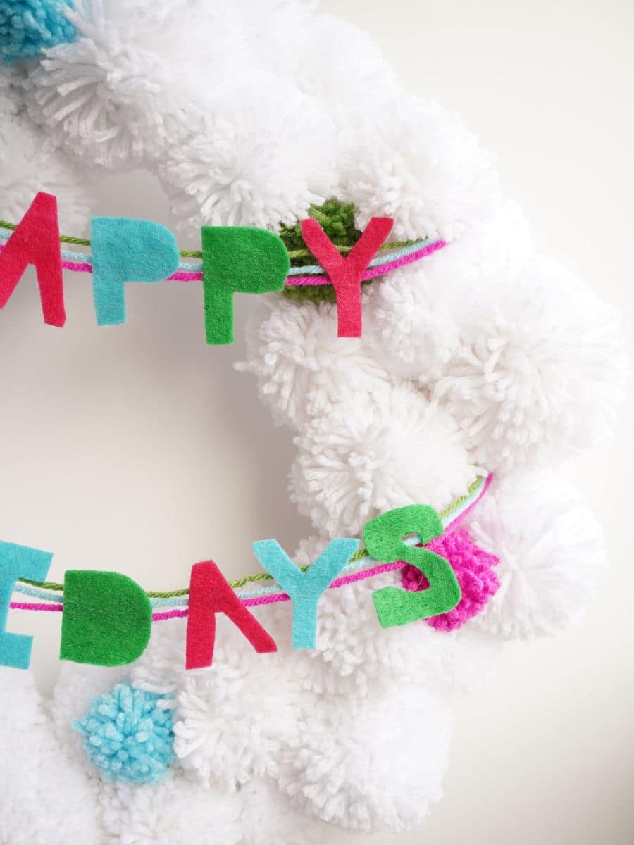 close up of happy holidays garland wrapped around white pom pom wreath