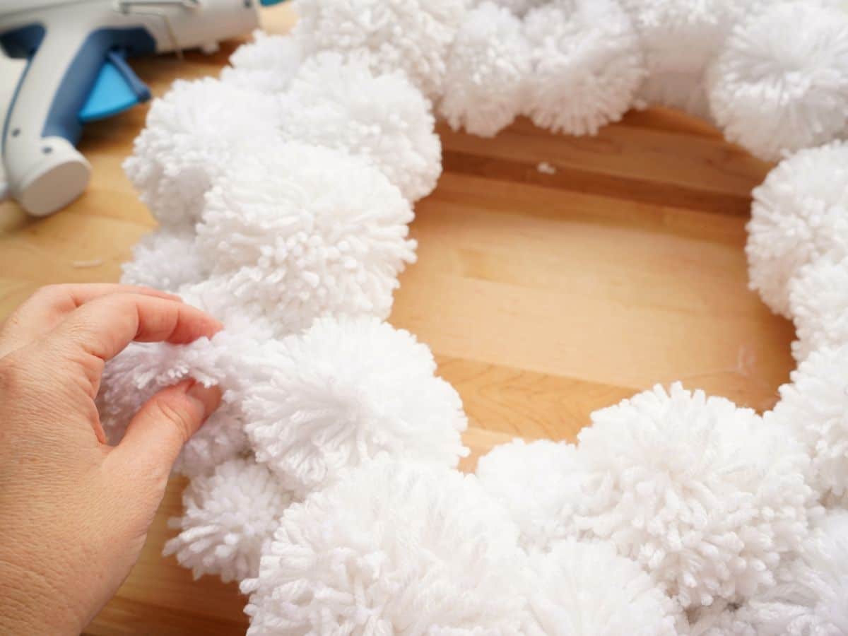 hand pressing pompom into pompom wreath