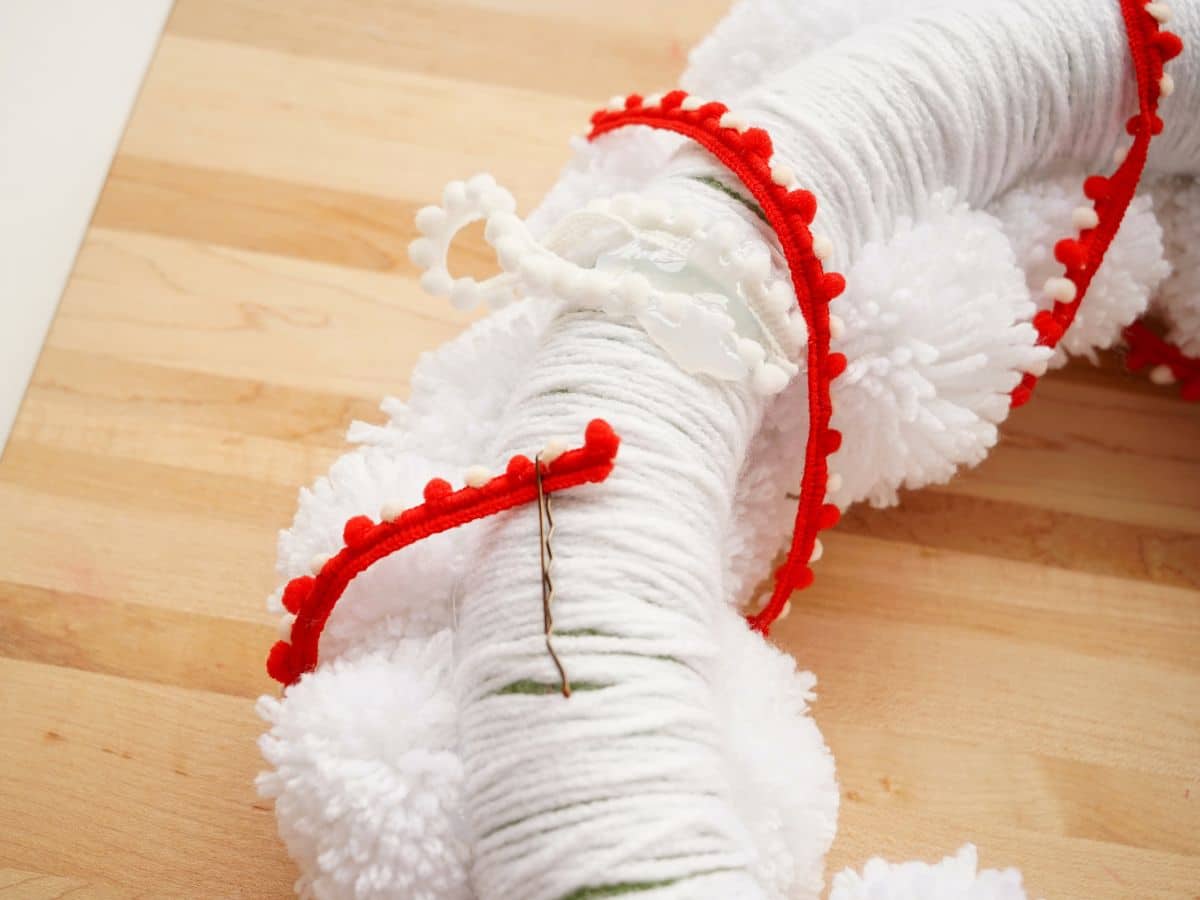 white christmas pompom wreath with red and white ribbon wrapped around it