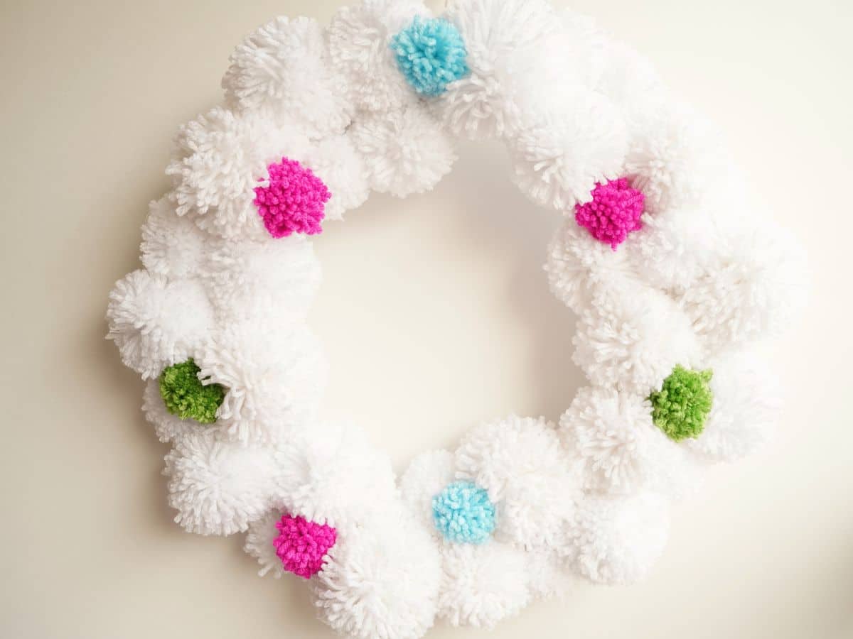 white pompom Christmas wreath with small colorful pompom decorations on wall