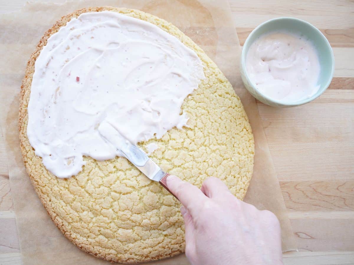 easter egg shaped sugar cookie with strawberry cream cheese spread on with offset spatula