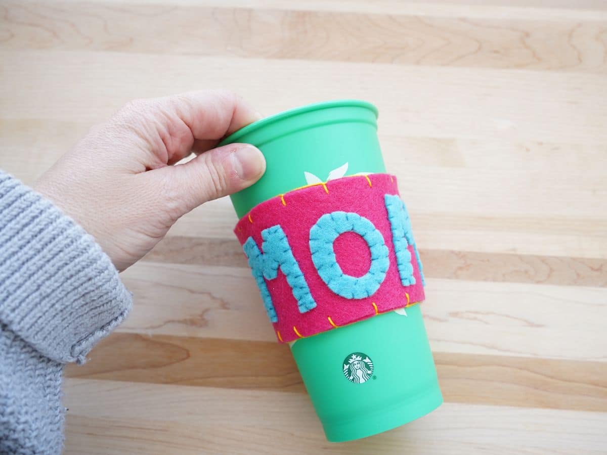 person's hand holding starbucks coffee cup with mother's day felt coffee cup sleeve on it