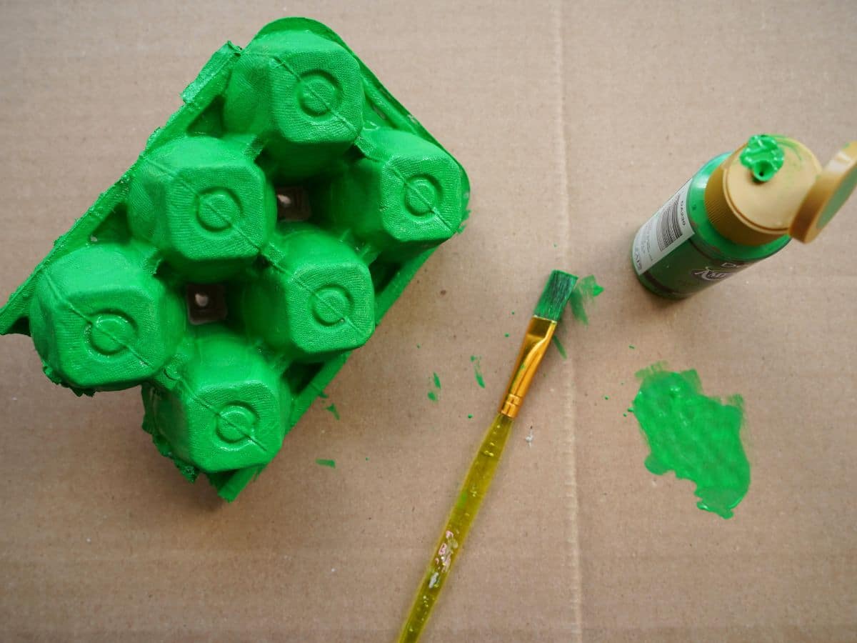 underside of egg carton painted green with paintbrush and bottle of paint