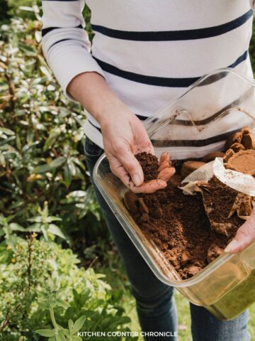 woman's hand in a container of coffee grounds standing in a garden
