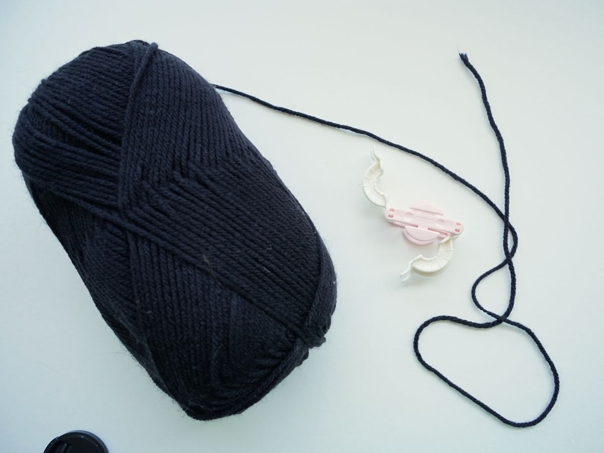 skien of black yarn with small pompom maker tool on table