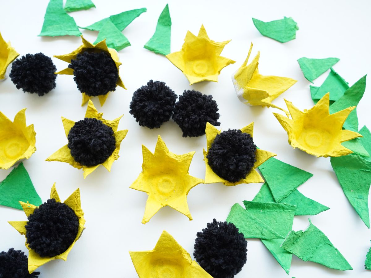 yellow egg carton flowers with black pompoms glued inside and pile of egg carton leaves