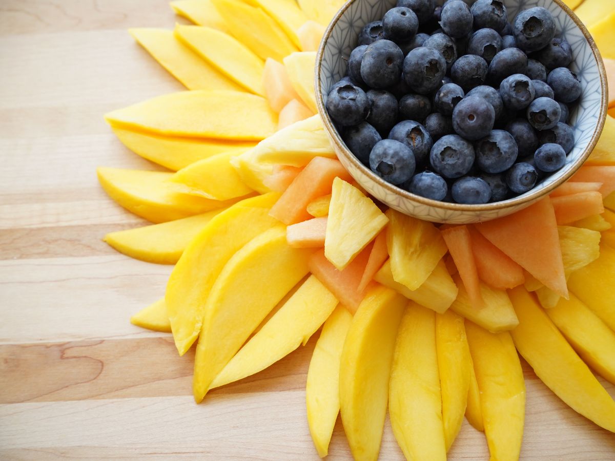 pineapple and cantaloupe slices arranged on to of mango slices and bowl of blueberries in center