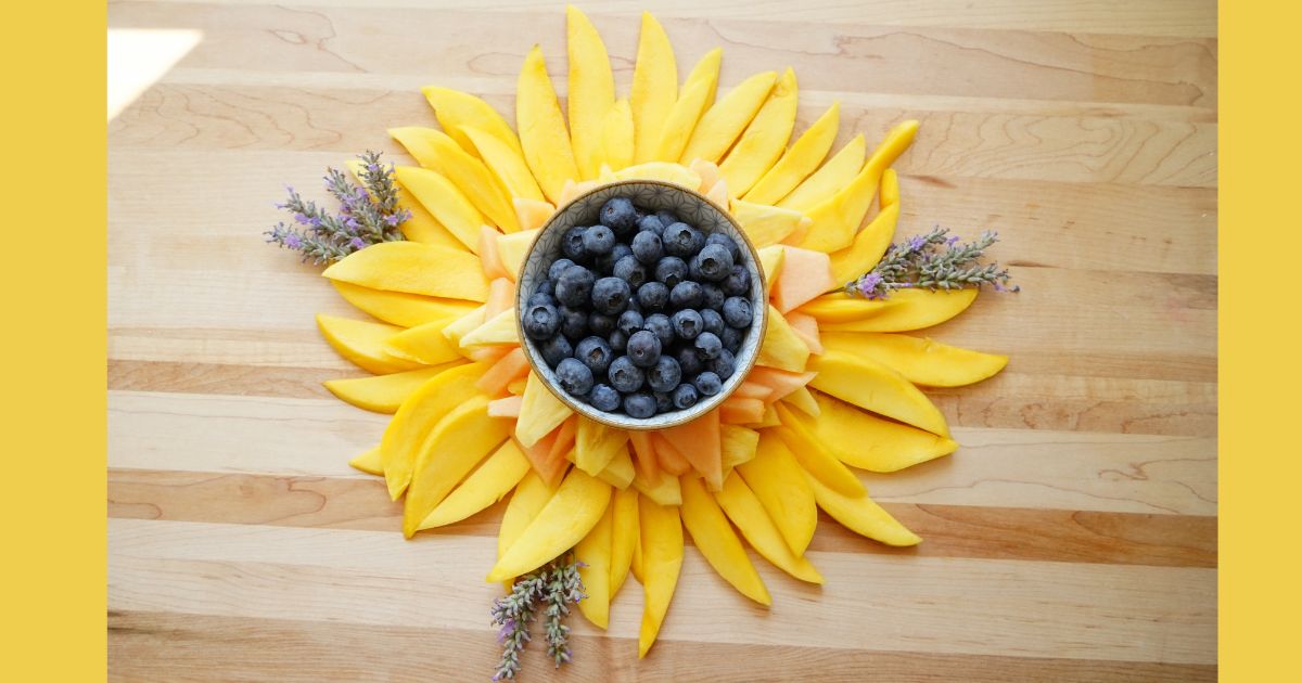 sunflower fruit tray made with mango slices, pineapple and cantaloupe with bowl of blueberries in middle and sprigs of lavender