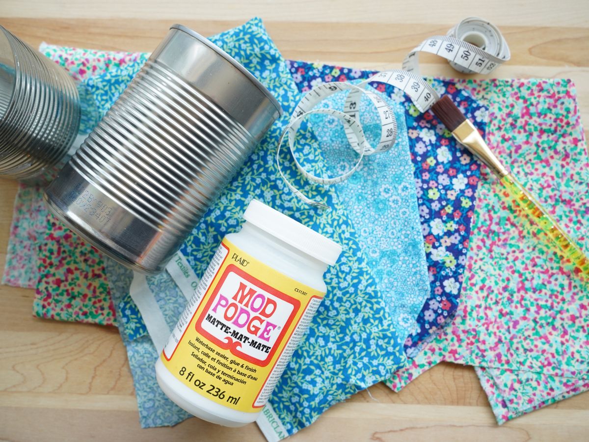 supplies for making tin can cup holders - fabric, paintbrush, tin cans, measuring tape and mod podge