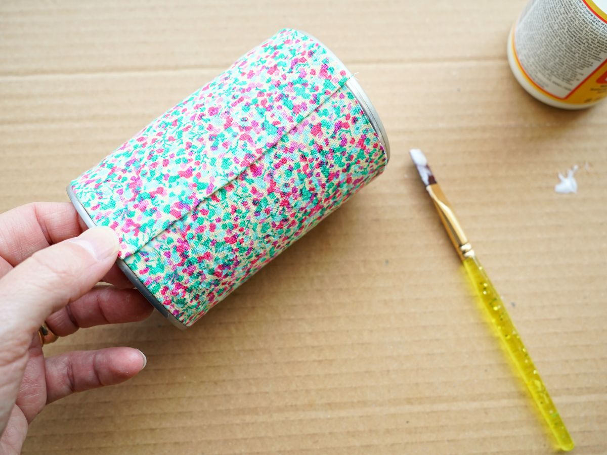 thumb pressing down seam in fabric wrapped tin can pencil cup