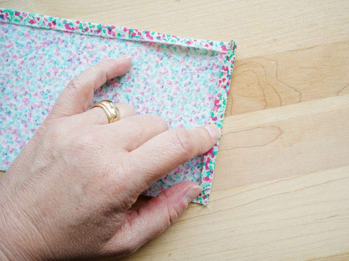 woman's hand finger pressing a hem on the fabric scrap for the tin can pencil cup