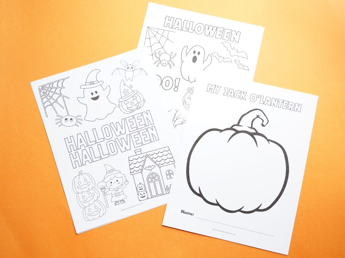 3 sheets of Halloween coloring pages sitting on orange table top