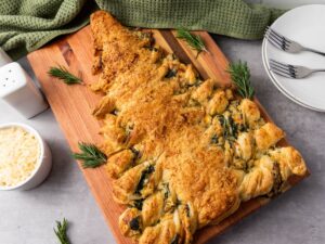 baked spinach dip filled christmas tree appetizer on wooden board with plates