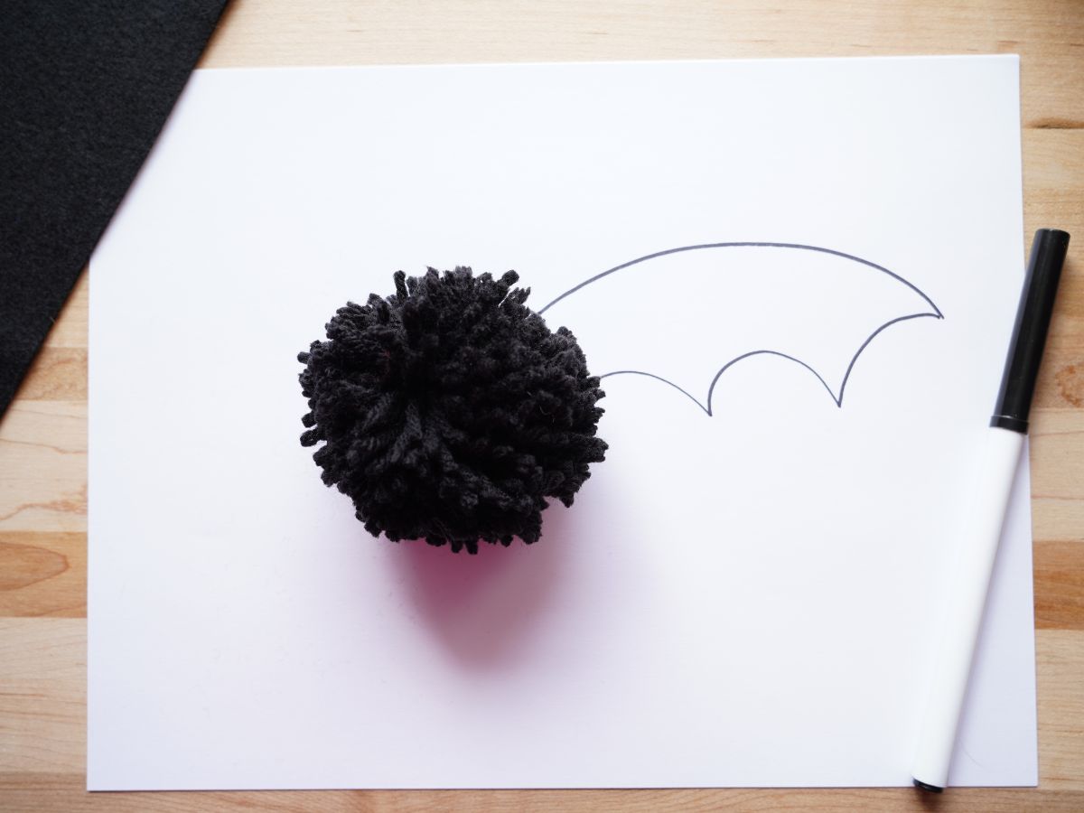 black pom pom on paper with bat wing drawn on with black marker