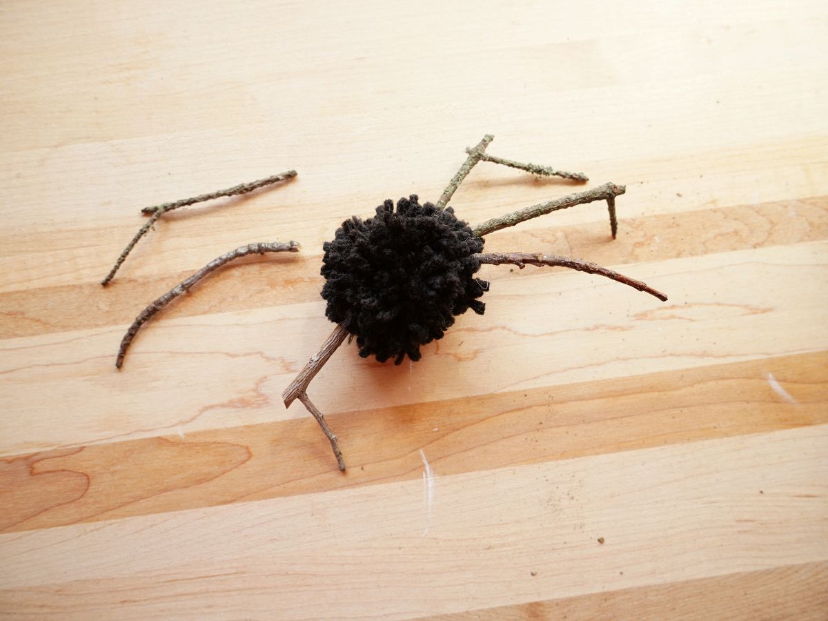 black pom pom spider with twig legs being glued on