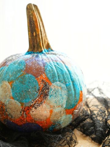 close up of diy glittery galaxy pumpkin sitting on black lace table cloth