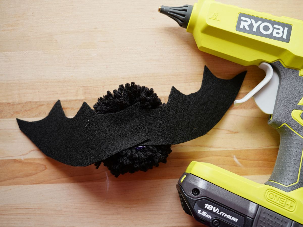 glue gun beside felt bat wings being glued on pompom bat