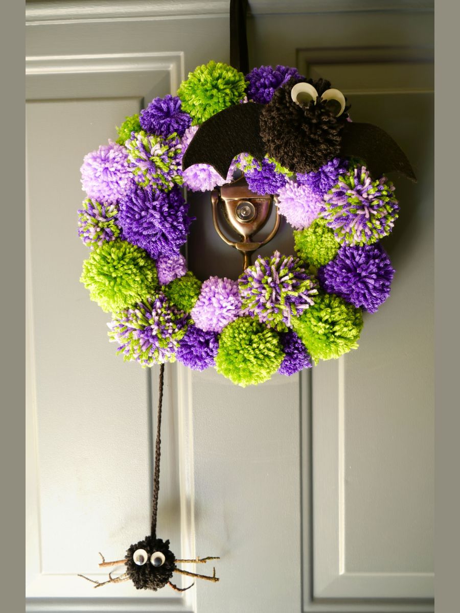 green and purple diy halloween pom pom wreath hanging on front door