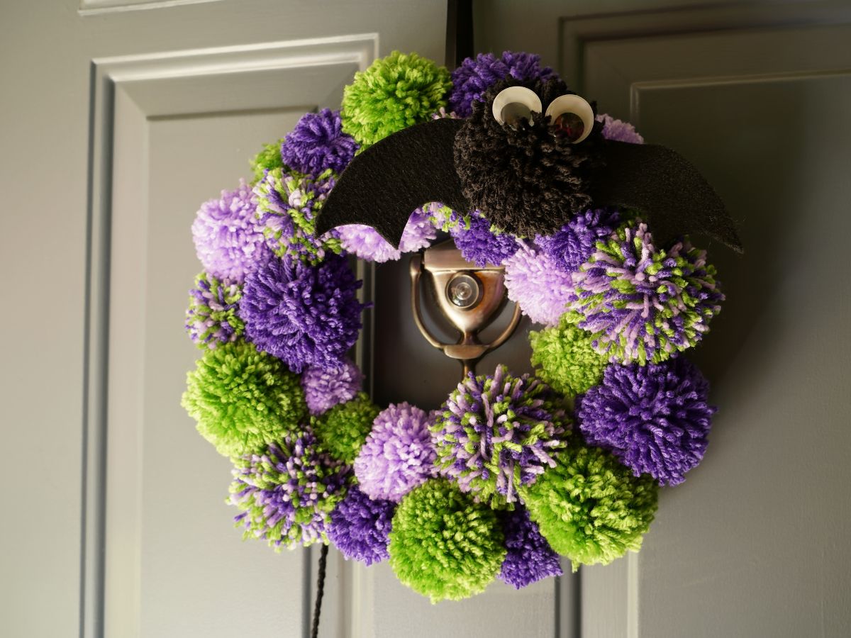 green and purple pom pom halloween wreath hanging on door with pom pom bat